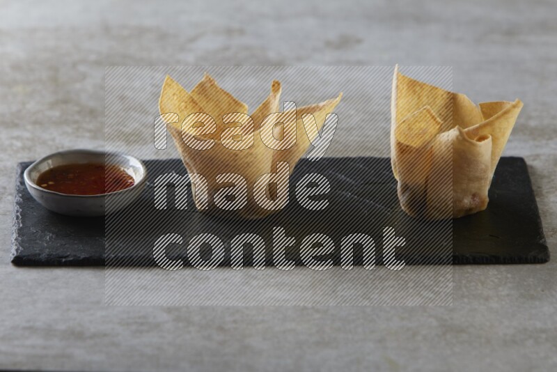 wonton cups with soy sauce ramkin on rectangle slate on grey textured counter top