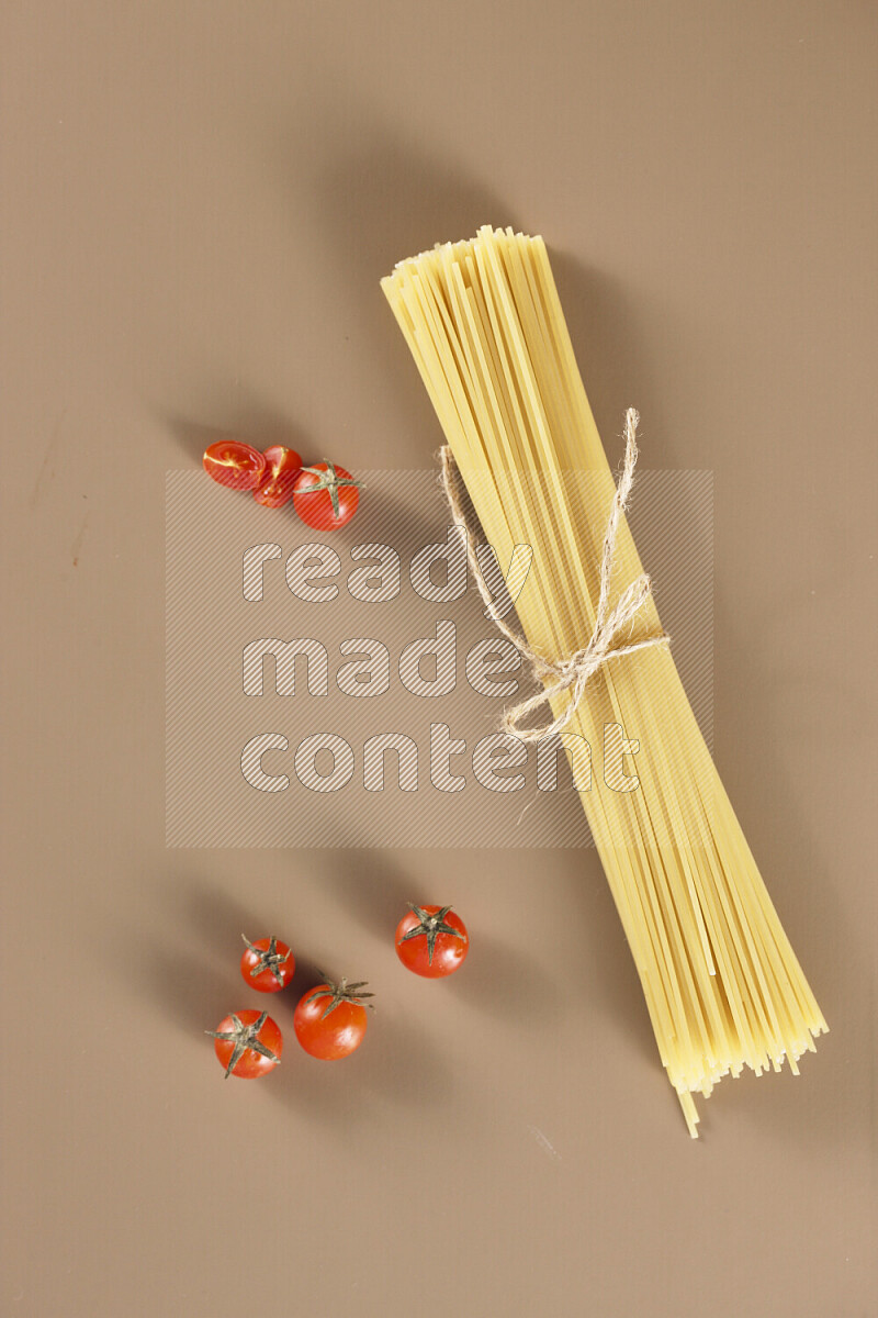 Raw pasta with different ingredients such as cherry tomatoes, garlic, onions, red chilis, black pepper, white pepper, bay laurel leaves, rosemary and cardamom on beige background