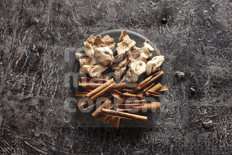 Ginger and cinnamon sticks on a black plate on textured black background