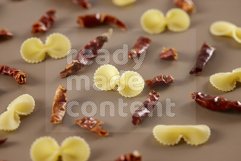 Raw pasta with different ingredients such as cherry tomatoes, garlic, onions, red chilis, black pepper, white pepper, bay laurel leaves, rosemary and cardamom on beige background