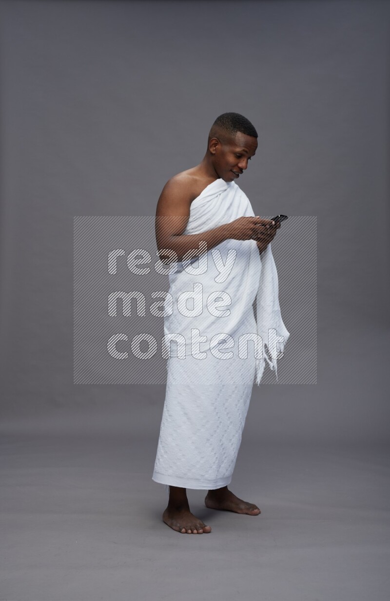 A man wearing Ehram Standing texting on phone on gray background
