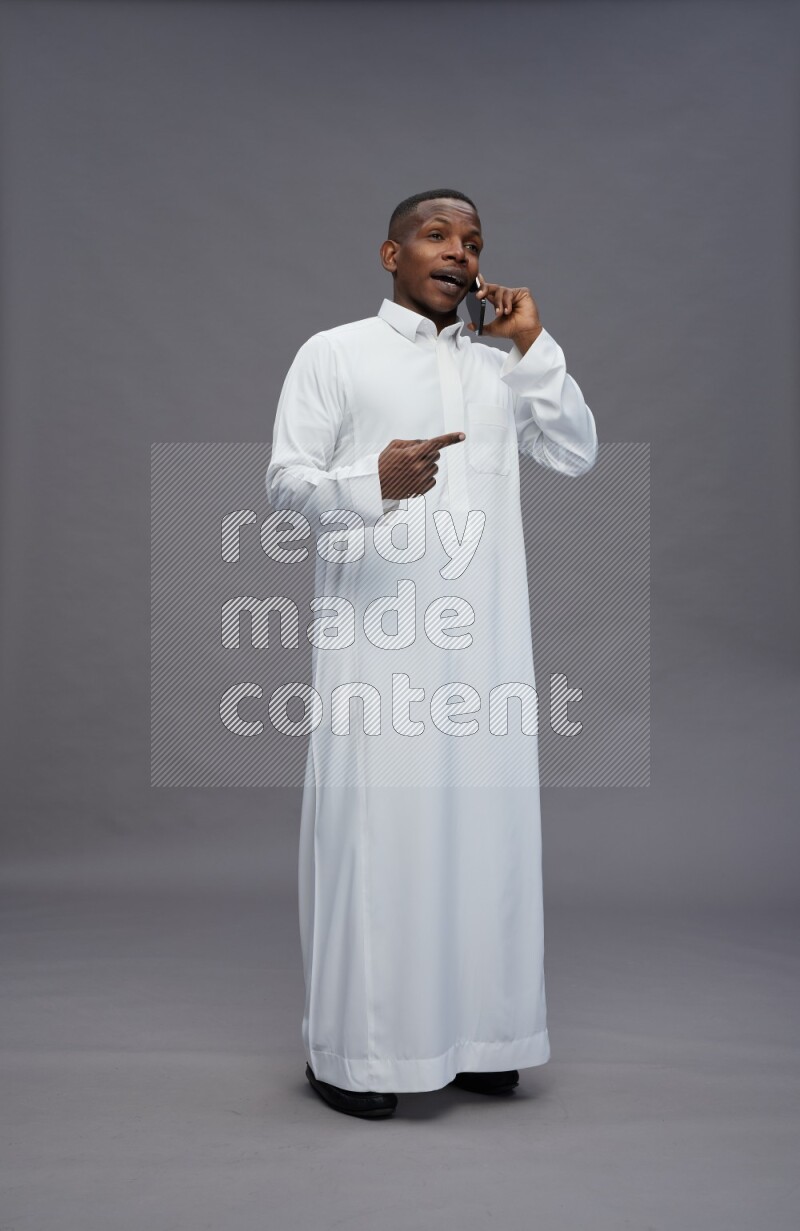 Saudi man wearing thob standing talking on phone on gray background