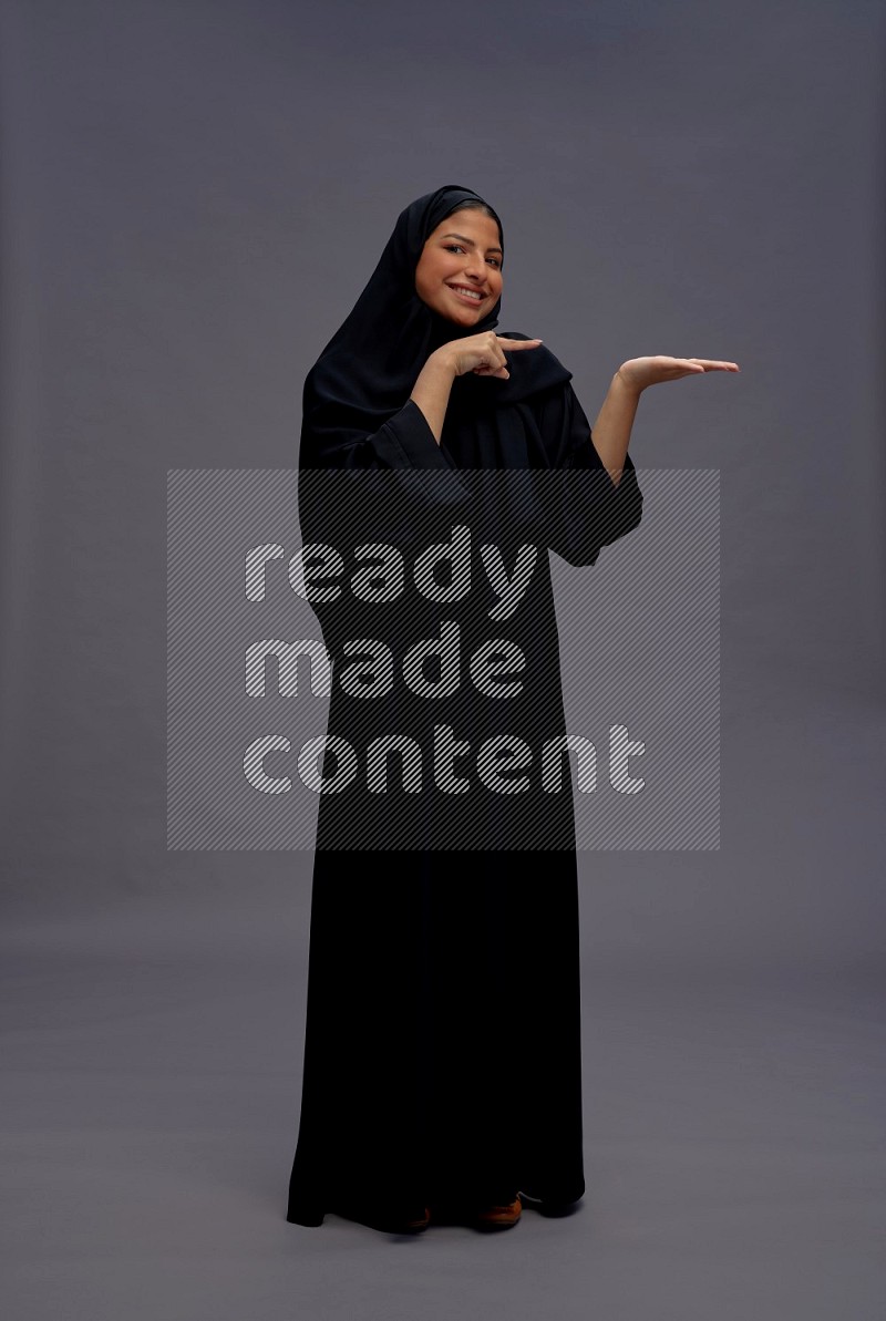 Saudi woman wearing Abaya standing interacting with the camera on gray background