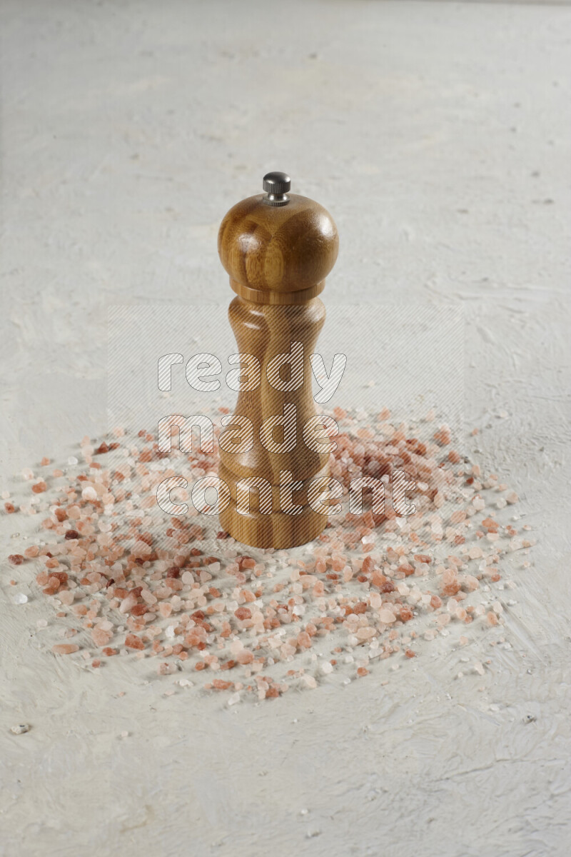 A wooden grinder standing upright and surrounded by coarse pink himalayan salt on white background