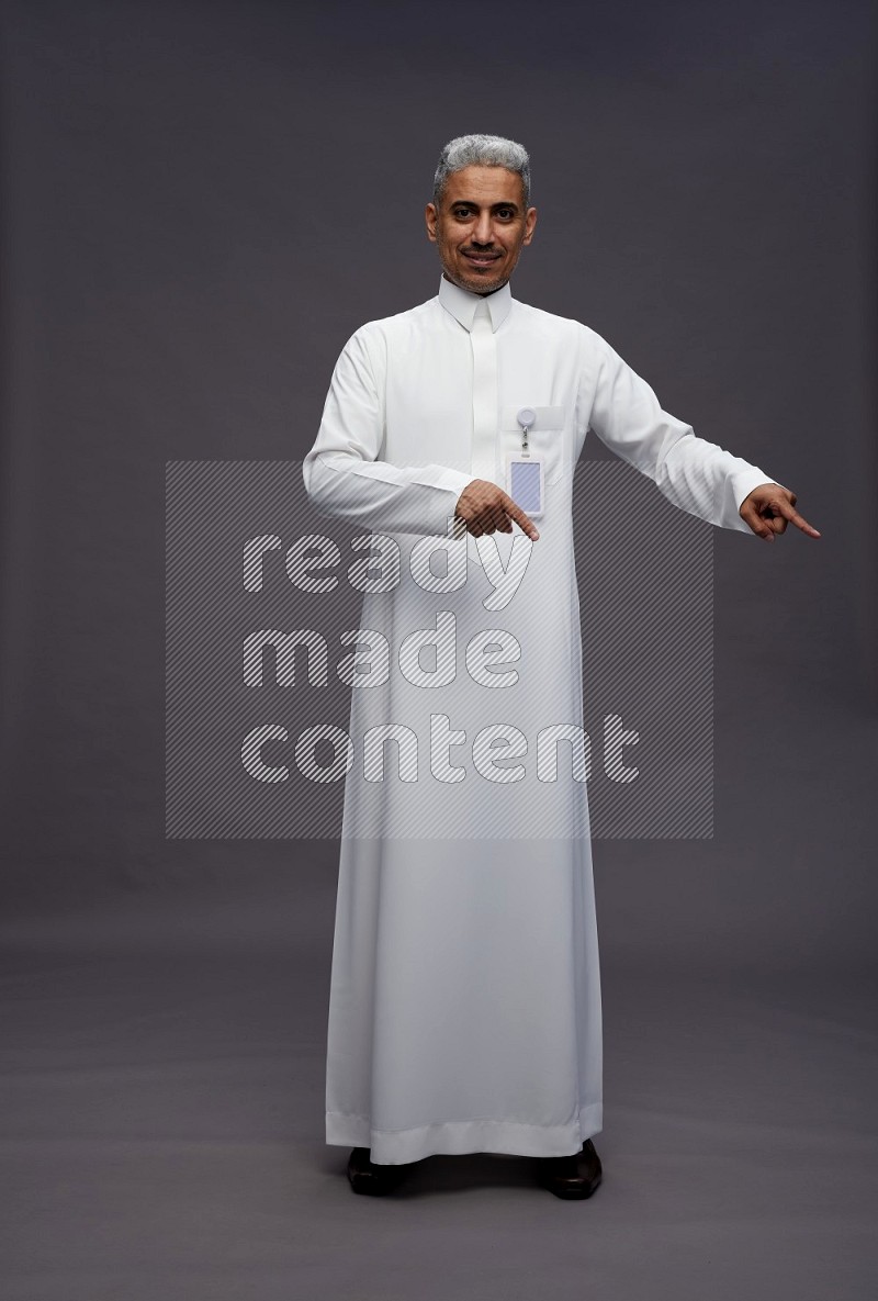 Saudi man wearing thob with pocket employee badge standing interacting with the camera on gray background