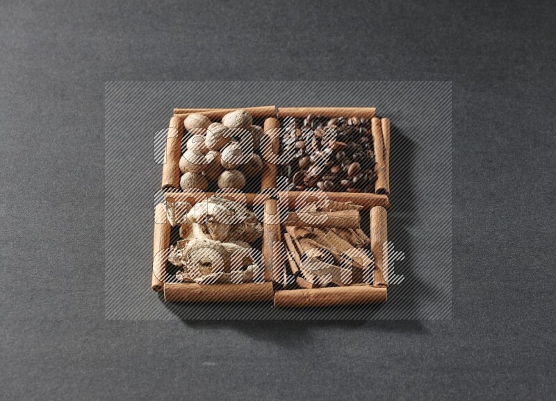 4 مربعات من عيدان القرفة ممتلئة بحبوب القهوة وقطع القرفة والزجبيل المجفف وجوزة الطيب على أرضية سوداء