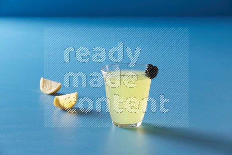 glass of lemon juice with berry on blue background