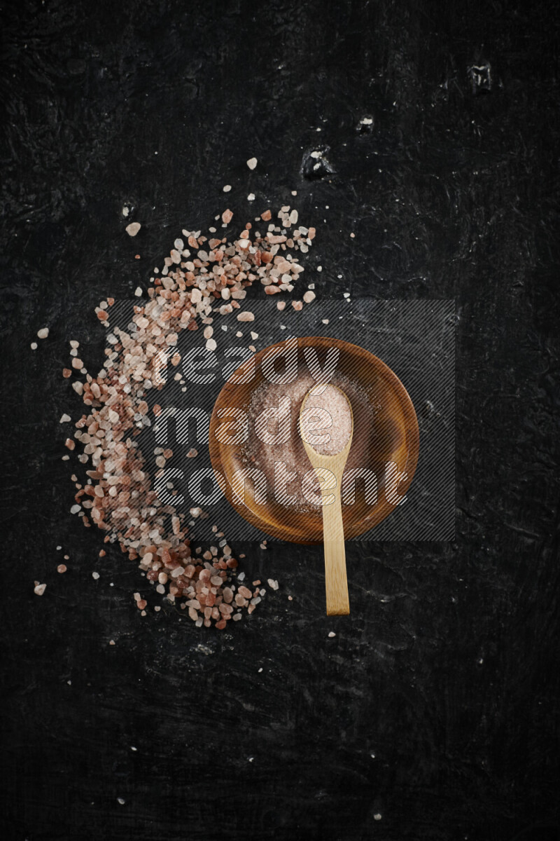 A pottery plate full of fine salt with bunch of coarse salt beside it on black background
