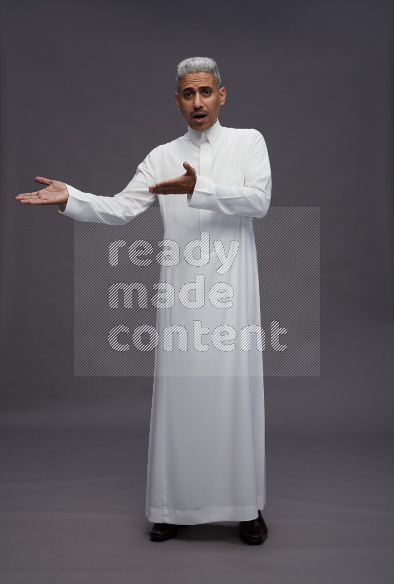 Saudi man wearing thob standing interacting with the camera on gray background