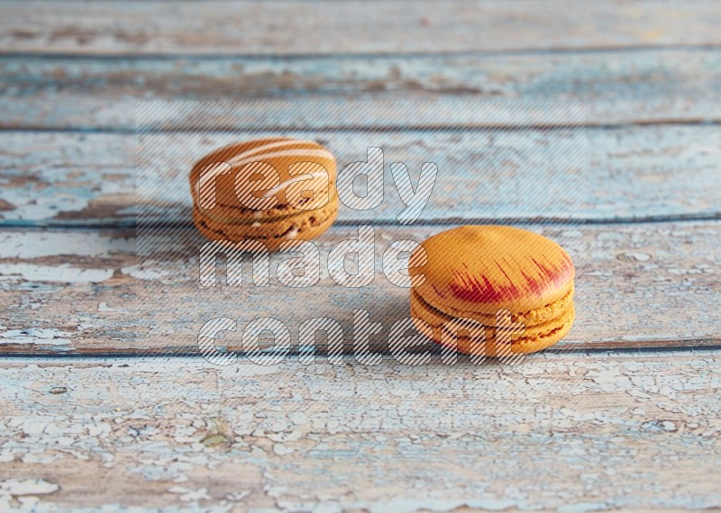 45º Shot of of two assorted Brown Irish Cream, and Orange Exotic macarons on light blue background