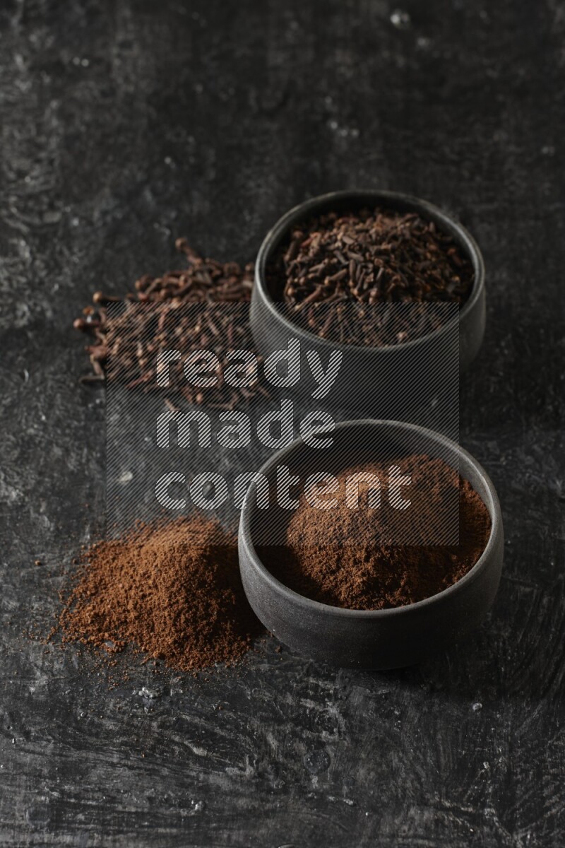 وعاءين من الفخار الأسود أحدهما ممتلئي بحبوب القرنفل والآخر ممتلئ ببودرة القرنفل على خلفية سوداء