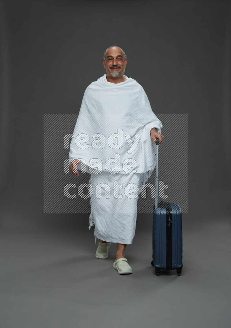 A man wearing Ehram Standing holding traveling bag on gray background