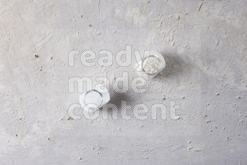 2 glass jars one is filled with table salt and the other with coarse sea salt on white background