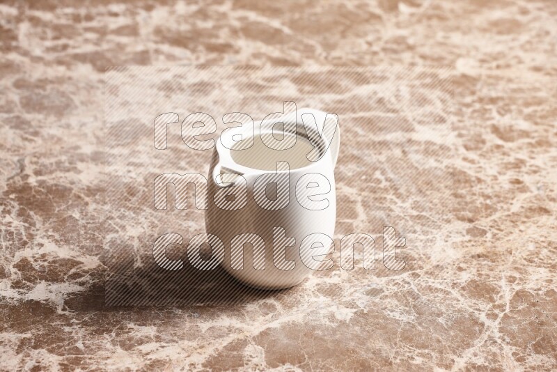 A ceramic milk jug on beige marble background