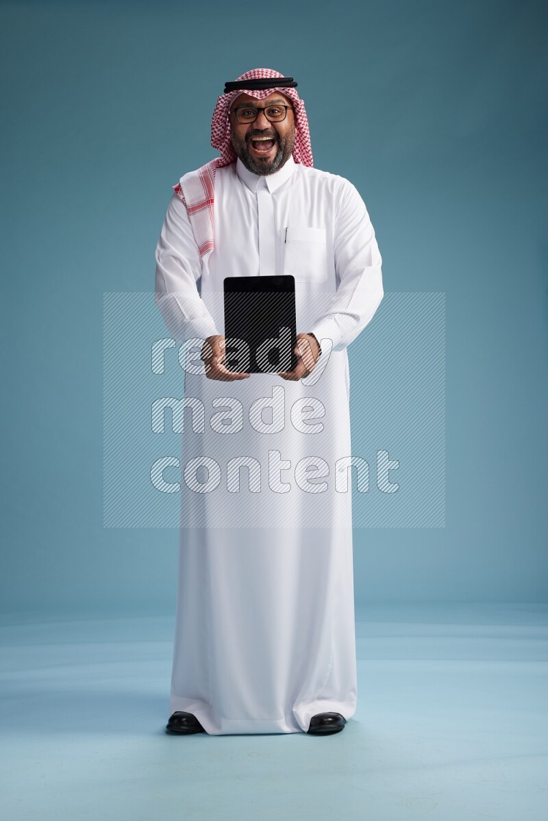 Saudi Man with shimag Standing holding a tablet on blue background