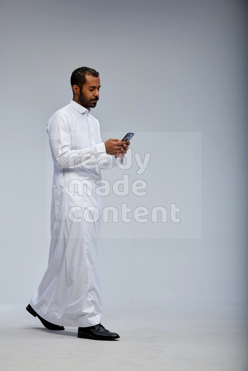 Saudi man wearing Thob standing texting on phone on Gray background