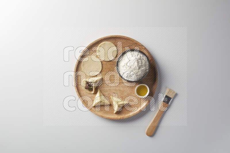 two closed sambosas and one open sambosa filled with meat while flour, and oil with oil brush aside in a wooden dish on a white background