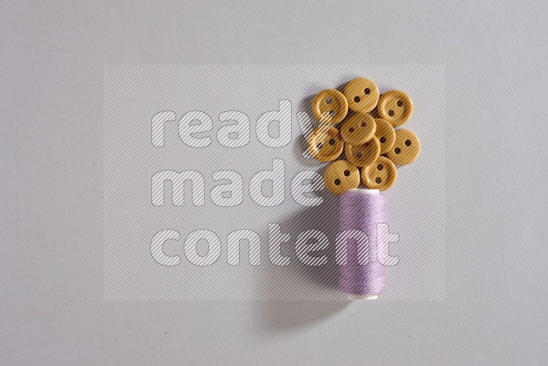 A purple sewing thread spool with colored buttons on grey background