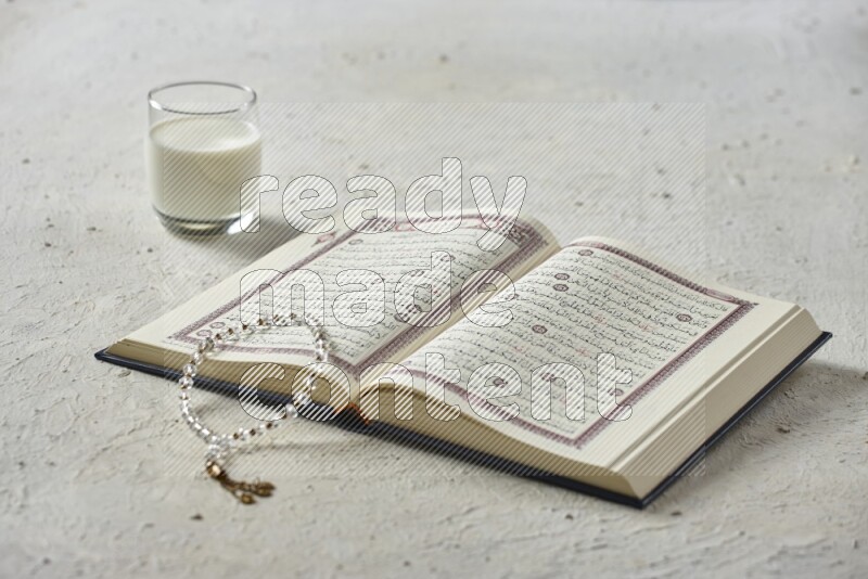 Quran with dates, prayer beads and different drinks all placed on textured white background