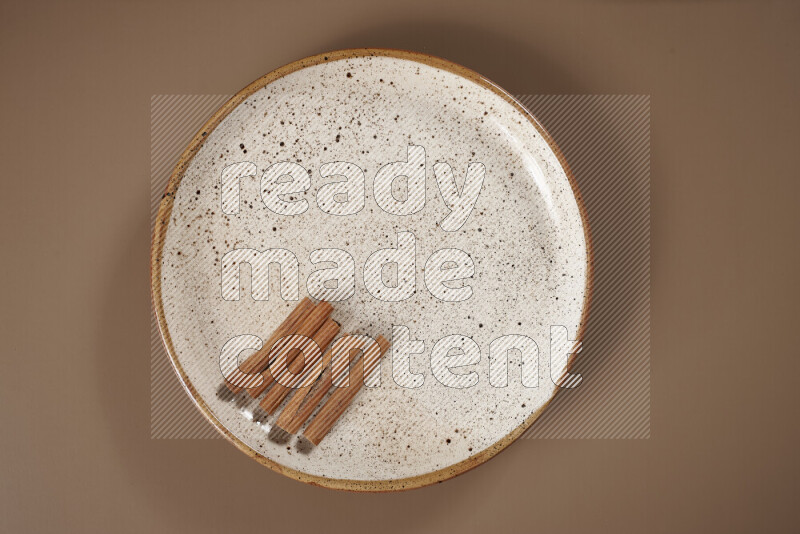 An assorted whole spices on a flat beige plate including fresh and dried ginger, cinnamon sticks, cardamom, turmeric fingers, cloves, star anise on a beige background