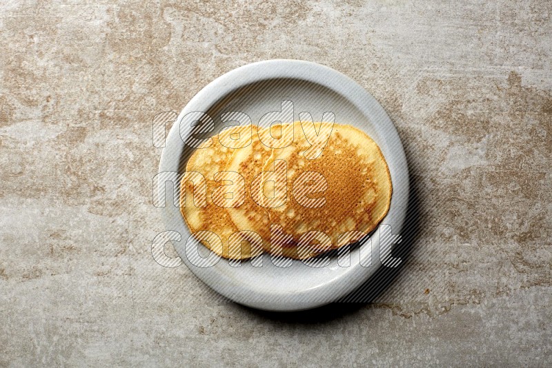 Three stacked plain pancakes in a grey plate on beige background