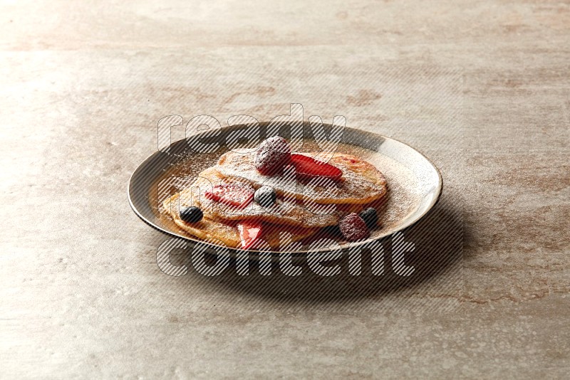 Three stacked mixed berries pancakes in a bicolor plate on beige background