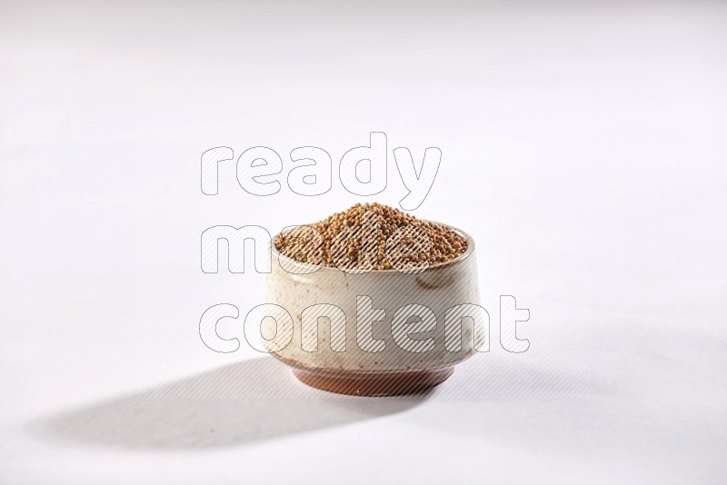 A beige pottery bowl full of mustard seeds on white flooring