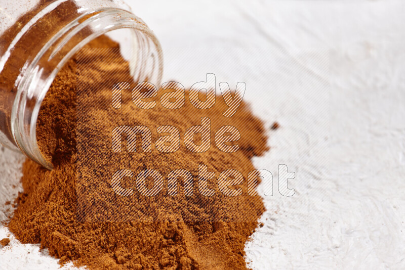 A glass jar full of ground paprika powder flipped with some spilling powder on white background