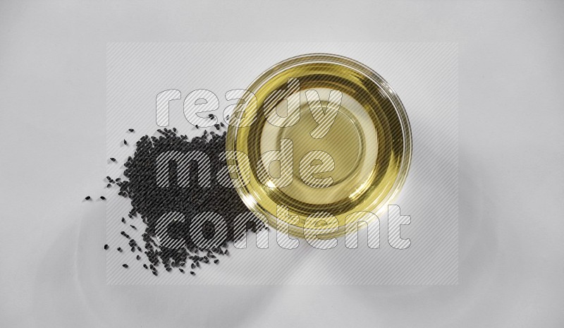 A glass bowl full of black seeds oil and black seeds beside it on a white flooring in different angles