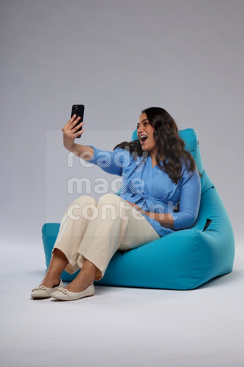 A woman sitting on a blue beanbag and taking selfie