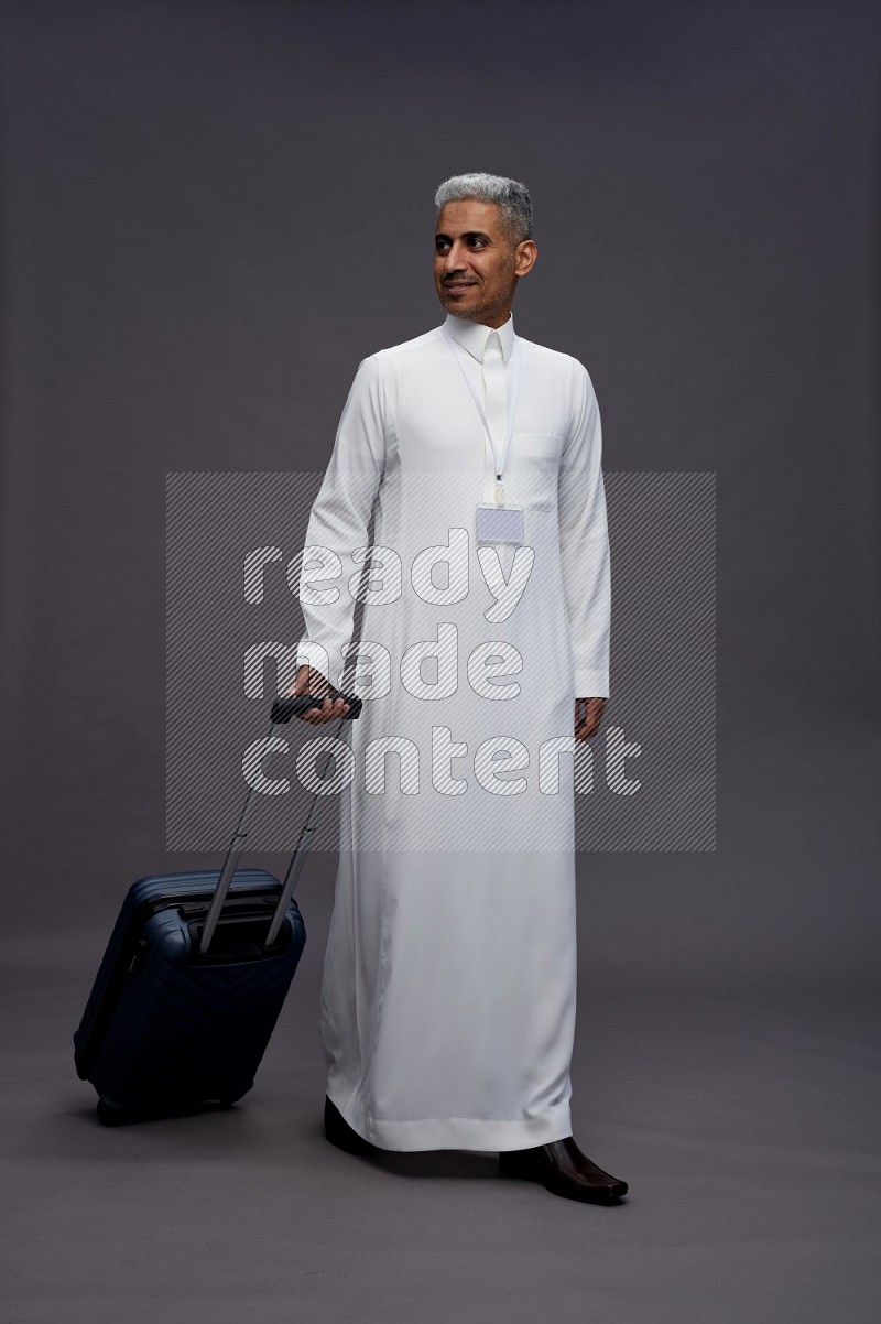 Saudi man wearing thob with neck strap employee badge standing holding bag on gray background