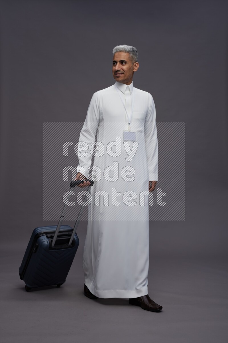 Saudi man wearing thob with neck strap employee badge standing holding bag on gray background