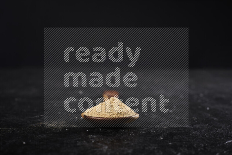 A wooden ladle full of ground ginger powder on black background