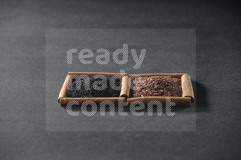 مربعان من أعواد القرفة ممتلئان ببذور الكتان وحبة البركة السوداء علي خلفية سوداء