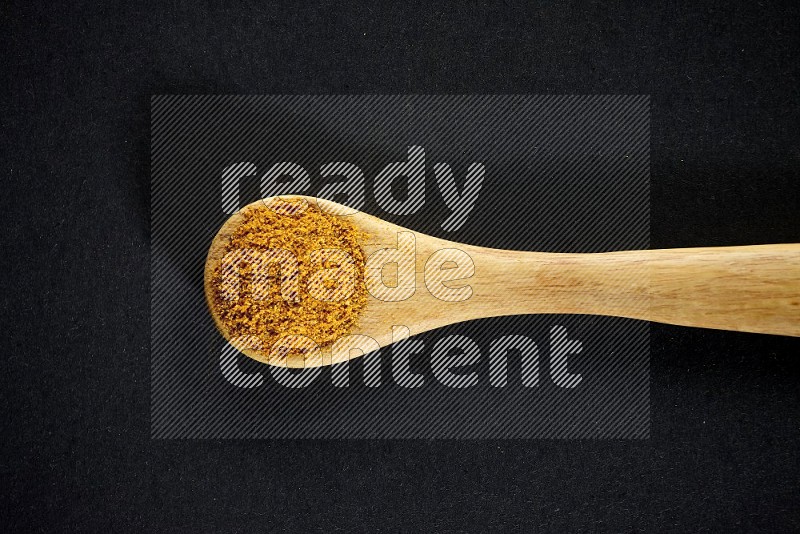 A wooden spoon full of turmeric powder on black flooring