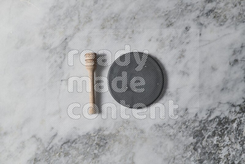 Black pottery plate with wooden honey dipper on the side on grey marble background