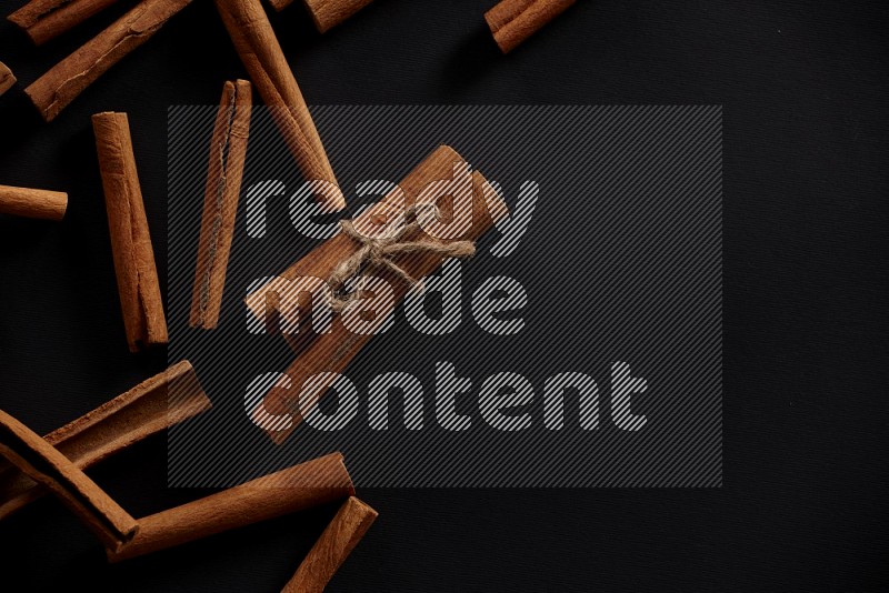 4 Cinnamon sticks stacked and bounded with more sticks in the background on black flooring