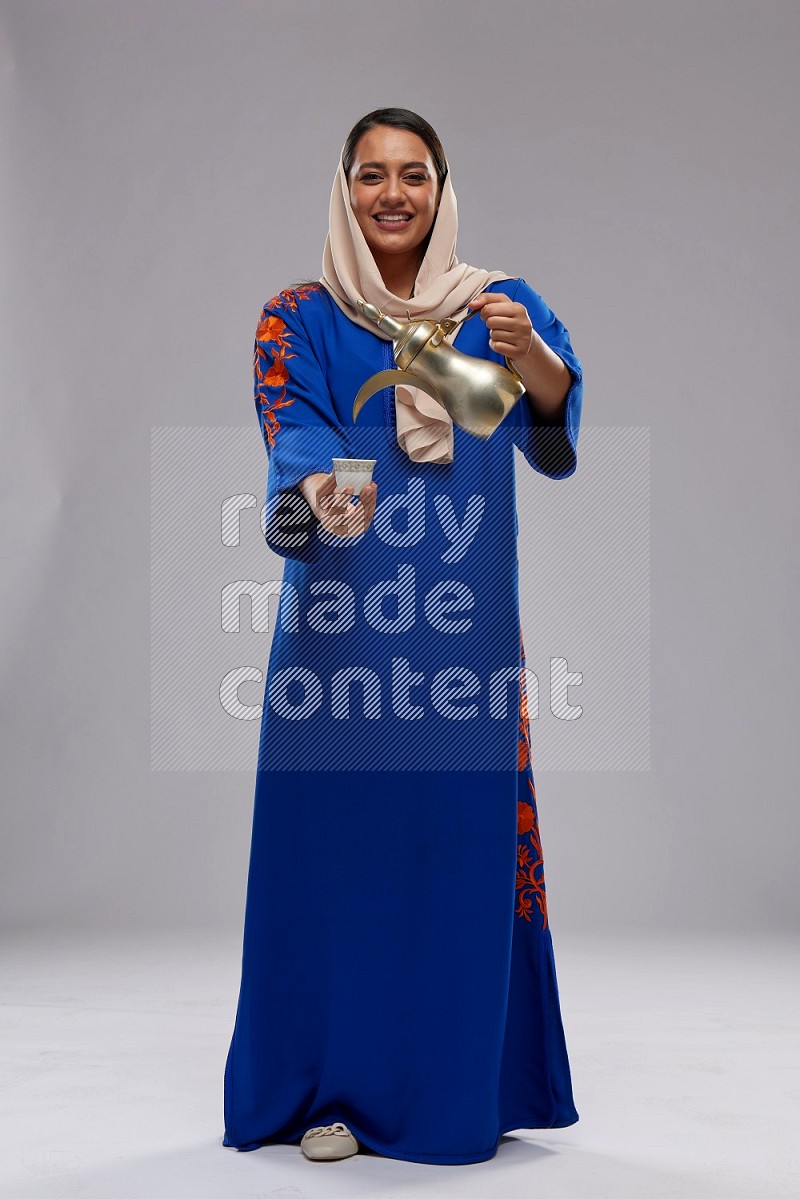 A Saudi woman standing wearing Jalabeya holding a coffee pot