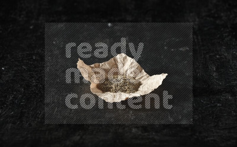 Cardamom powder in a crumpled piece of paper on textured black flooring