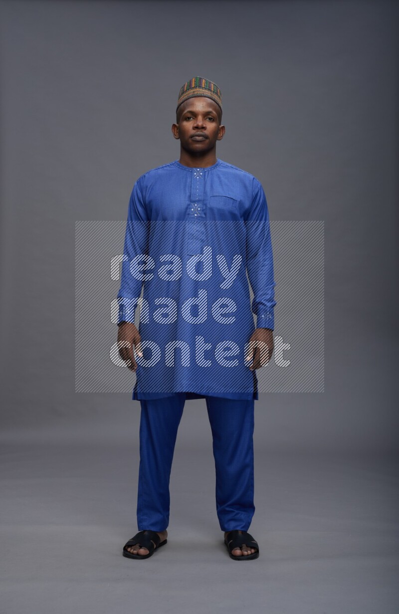 Man wearing Nigerian outfit standing interacting with the camera on gray background