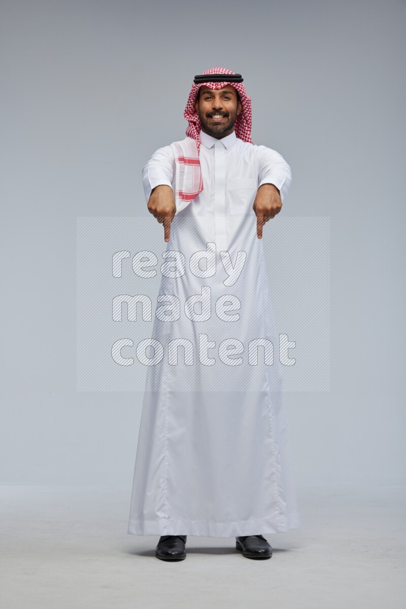 Saudi man Wearing Thob and shomag standing interacting with the camera on Gray background