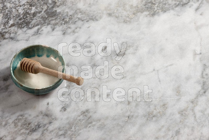 Multicolored Pottery bowl with wooden honey handle in it, on grey marble flooring, 65 degree angle