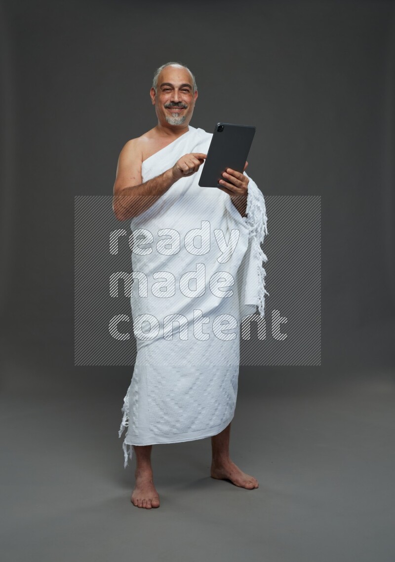 A man wearing Ehram Standing working on tablet on gray background