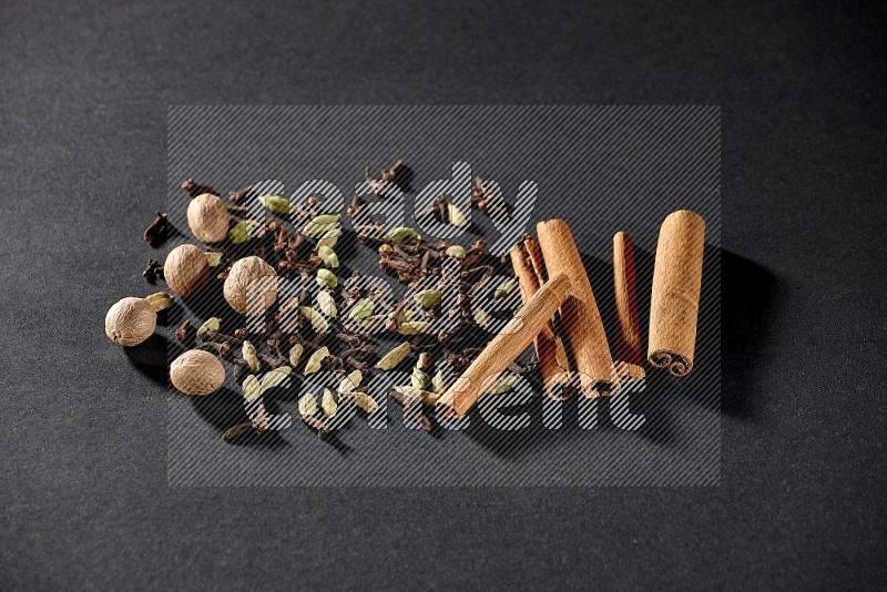 Cardamom, cloves, nutmeg and cinnamon sticks on black flooring