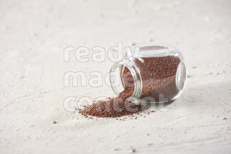 A glass spice jar full of garden cress seeds and jar is flipped with fallen seeds on a textured white flooring