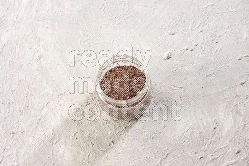 A glass jar full of flax seeds on a textured white flooring