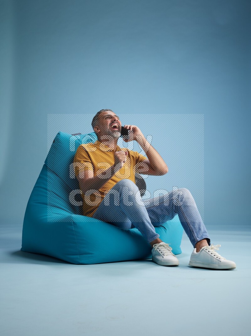 A man sitting on a blue beanbag and talking on the phone