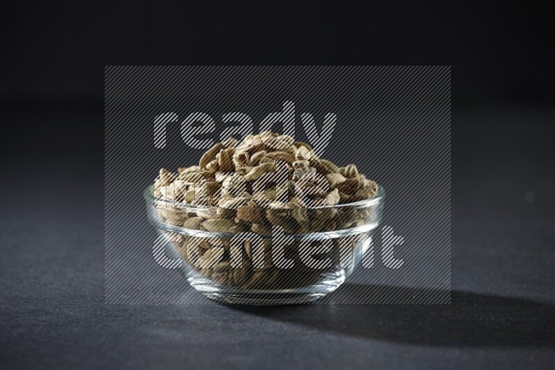 A glass bowl full of cardamom on black flooring