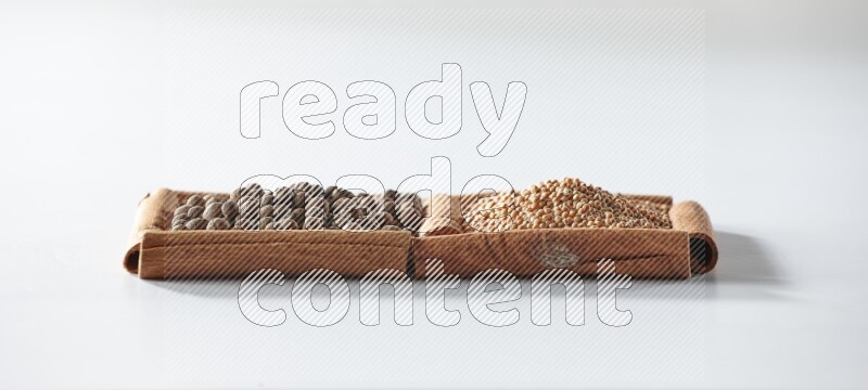 مربعان من أعواد القرفة ممتلئان بحبوب الخردل وحبوب بهار الفلفل الحلو علي خلفية بيضاء