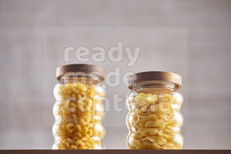 Raw pasta in glass jars on beige background